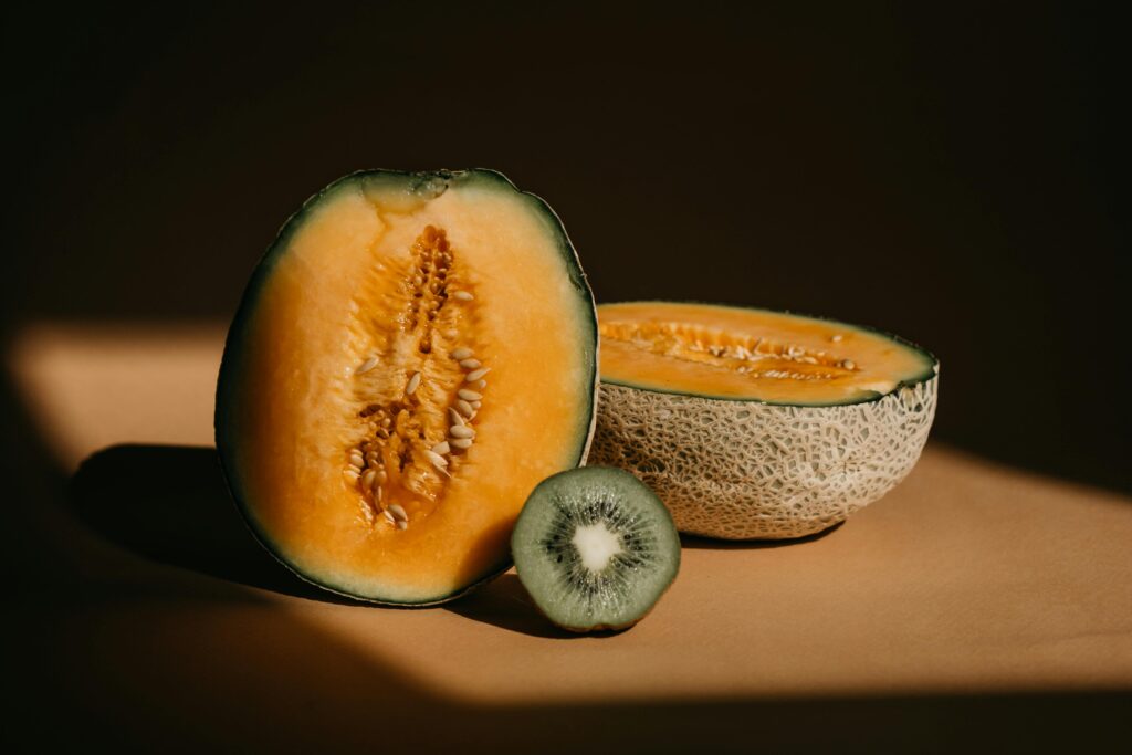 Close-up of sliced melon and kiwi fruit with dramatic play of light and shadow.